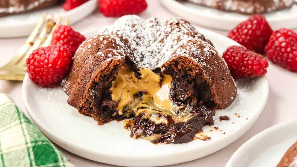 A chocolate lava cake with a peanut butter center is cut open on a white plate, garnished with powdered sugar and fresh raspberries.