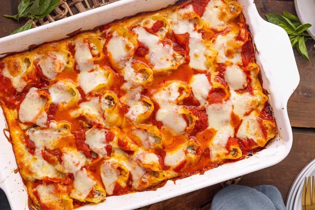A baked lasagna in a white rectangular dish, topped with melted cheese and tomato sauce, sits on a wooden table&mdash;perfect for a hearty pasta dinner.