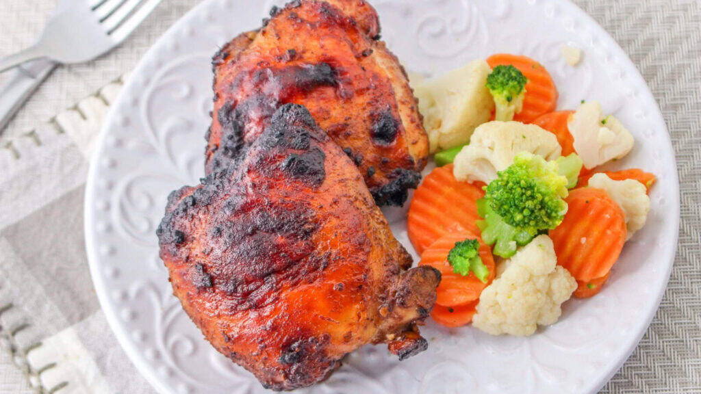 A white plate with two pieces of grilled chicken and a side of steamed mixed vegetables, including carrots, broccoli, and cauliflower.