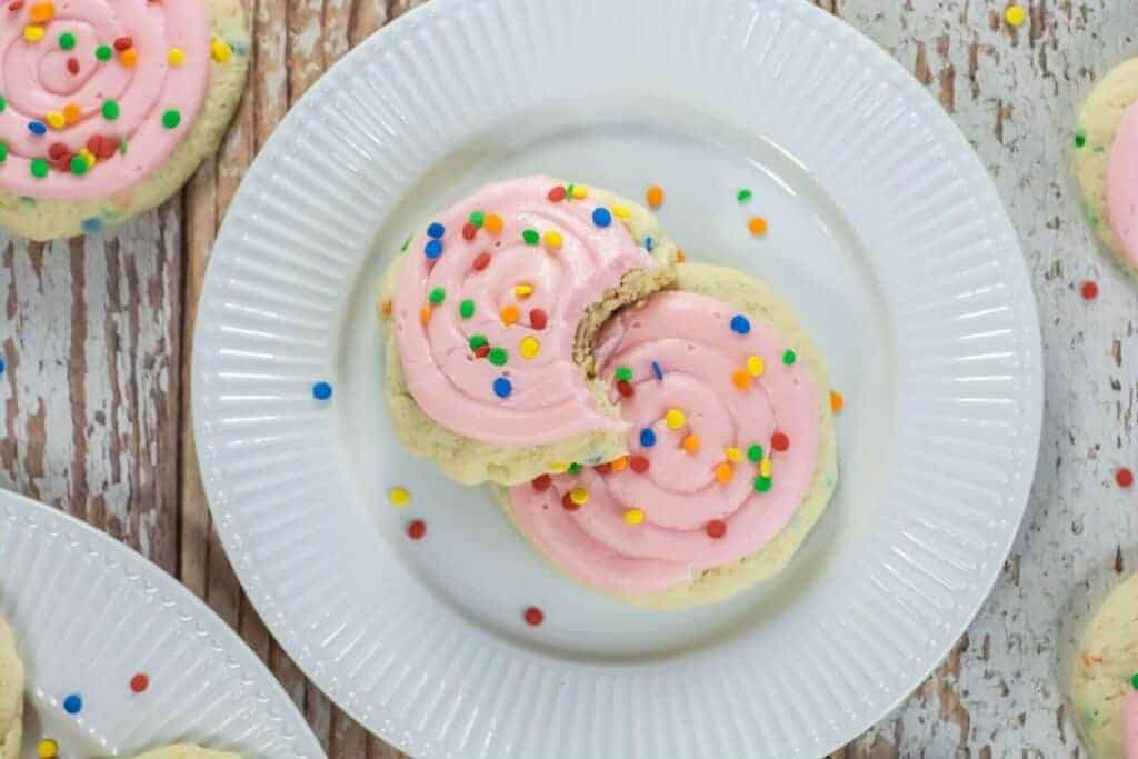 Two Crumbl-Style Confetti Cake Cookies on a white plate; one cookie has a bite taken out of it.