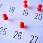 A close-up of a February calendar with red pushpins marking the dates 18, 19, 20, and 26.