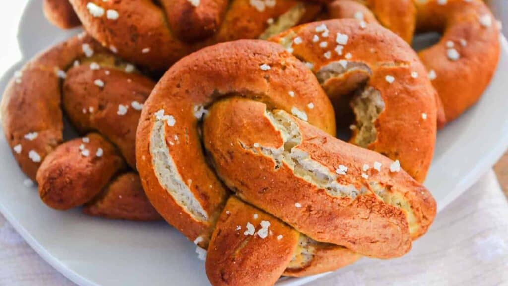 A plate of soft pretzels topped with coarse salt on a white surface.