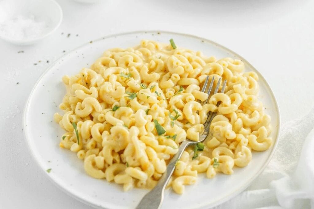 A plate of macaroni and cheese, one of the tastiest instant pot dishes, is garnished with chopped herbs, with a fork resting on the plate.