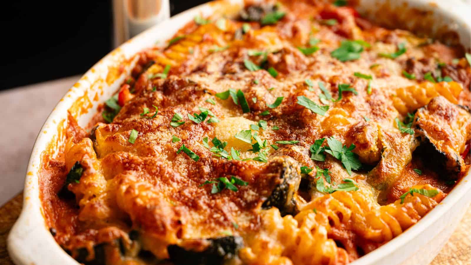 Baked pasta casserole topped with melted cheese, tomato sauce, and fresh parsley in a white dish.
