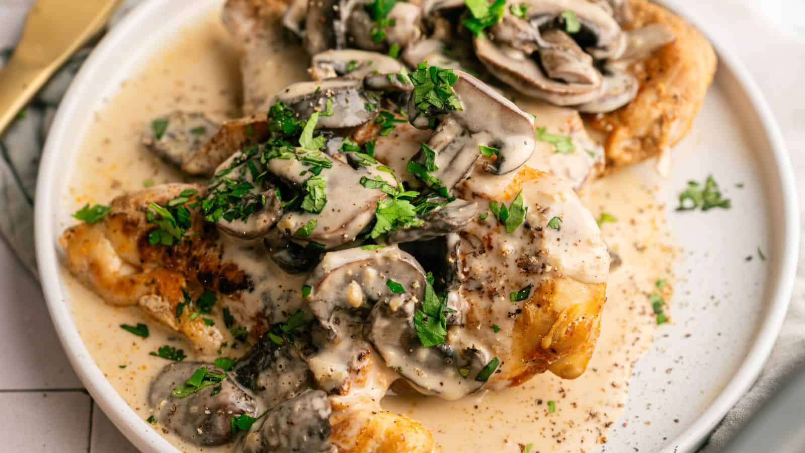 Plate of chicken covered in a creamy mushroom sauce, garnished with chopped parsley.