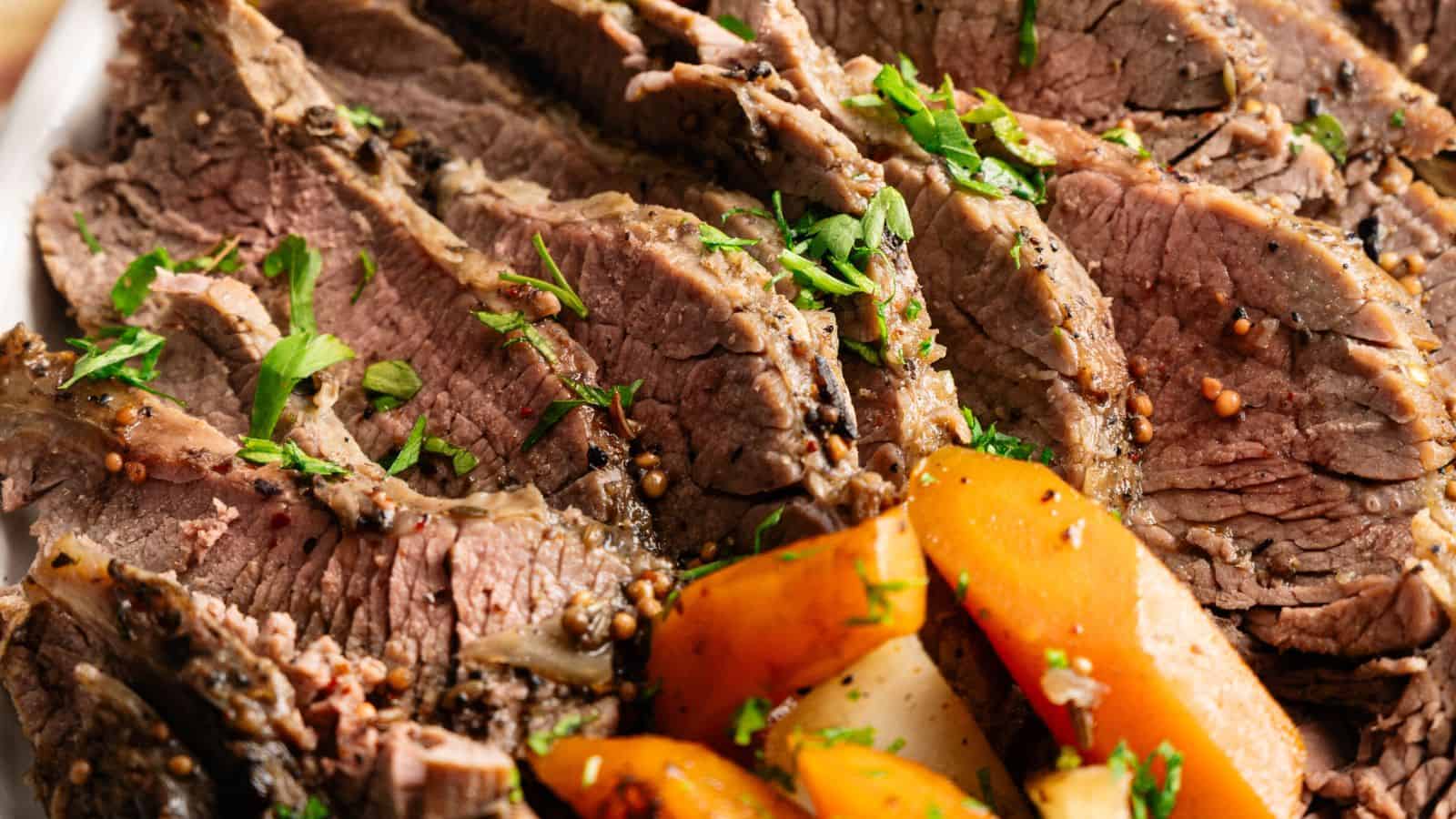 Sliced cooked beef garnished with chopped herbs, served with cooked carrots and potatoes.
