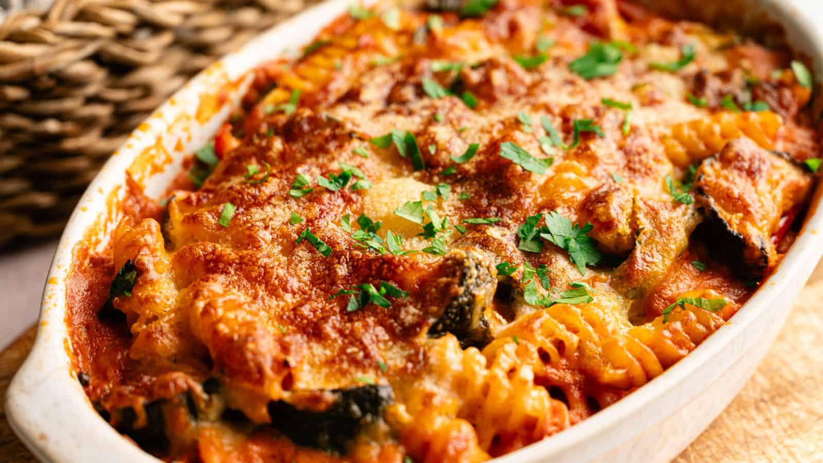 Baked pasta casserole with rotini noodles, tomato sauce, melted cheese, and chopped parsley in a white dish.
