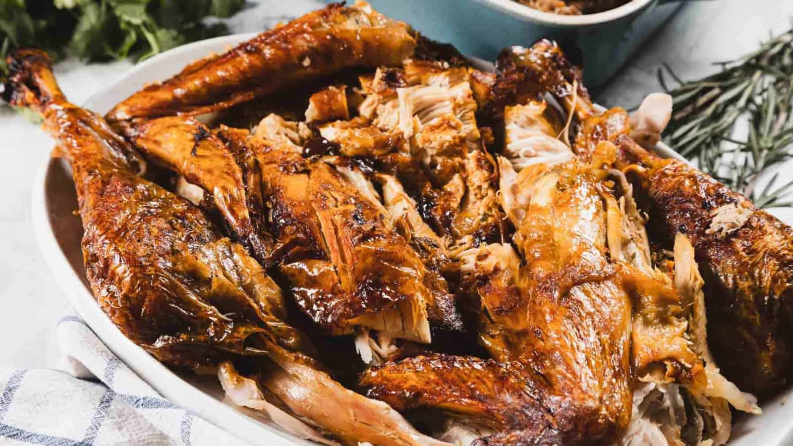 Platter of roasted, carved turkey pieces with crispy, golden brown skin on a white dish.