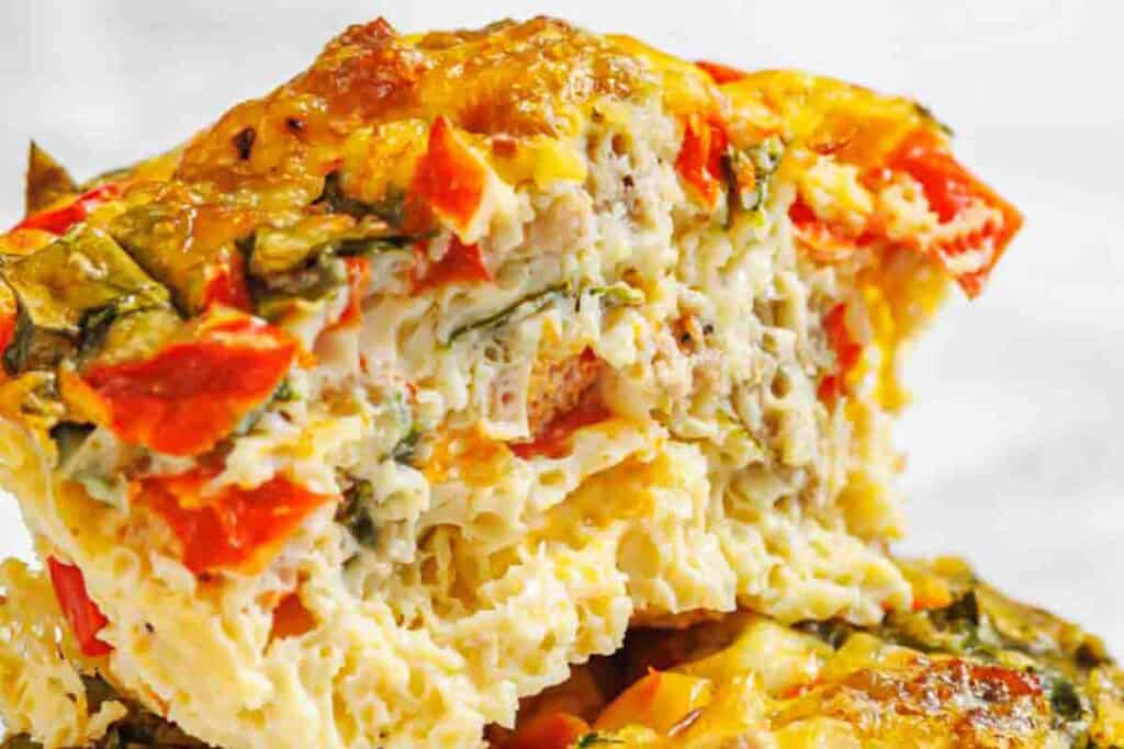 Close-up of a sliced egg muffin showing visible pieces of red bell pepper, leafy greens, and melted cheese.