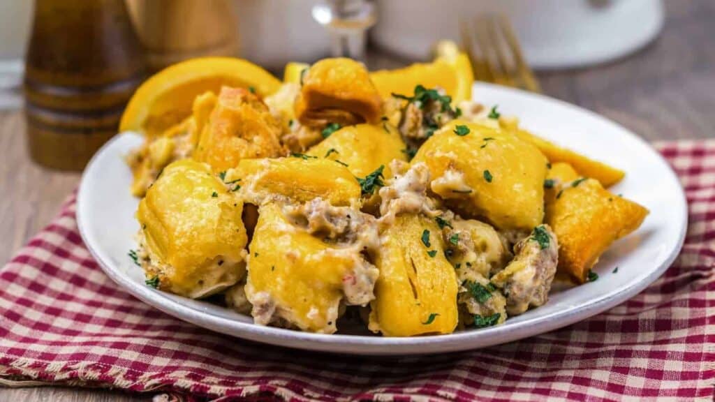 A white plate of gnocchi topped with a creamy sauce and herbs sits on a red checkered cloth with lemon wedges in the background.