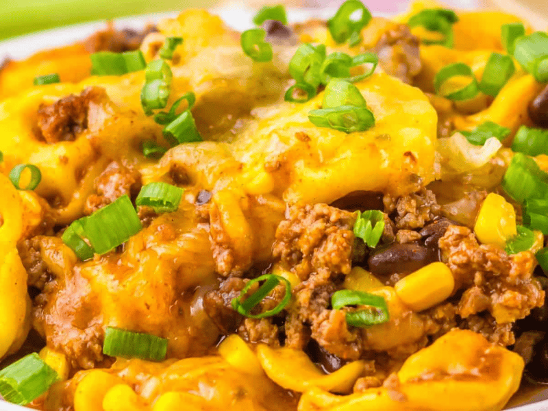Close-up of a Beef Enchilada Tortellini dish topped with ground meat, corn, black beans, and chopped green onions.