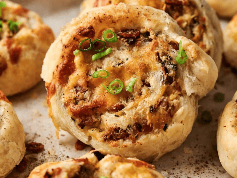 Close-up of baked puff pastry pinwheels filled with cheese, herbs, and finely chopped toppings, garnished with sliced green onions.