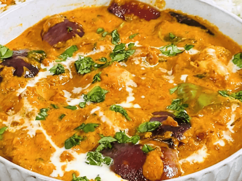 A bowl of creamy chicken tikka masala garnished with fresh herbs, served alongside a dish of rice.