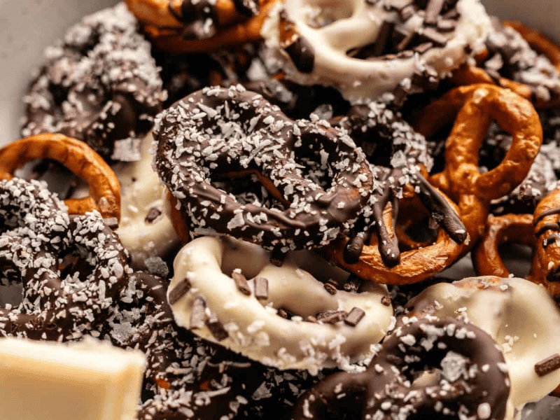 A bowl of pretzels coated in dark and white chocolate, topped with shredded coconut and chocolate sprinkles.