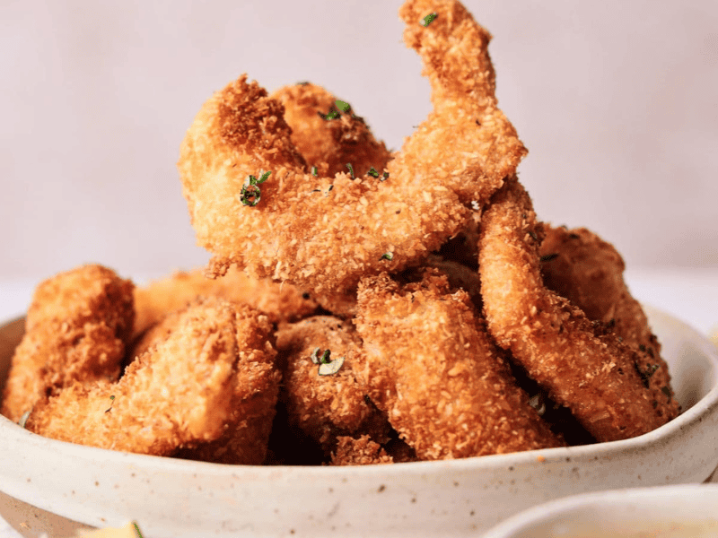 A bowl filled with golden-brown, breaded and fried shrimp, garnished with chopped herbs.