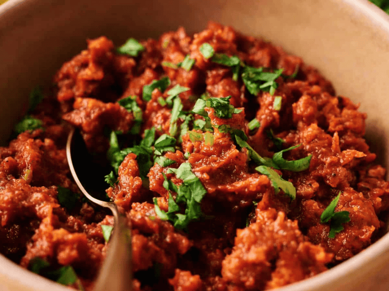 A plate of chickpea salad with chopped red onion, roasted red peppers, capers, almonds, and fresh herbs, served with a spoon.