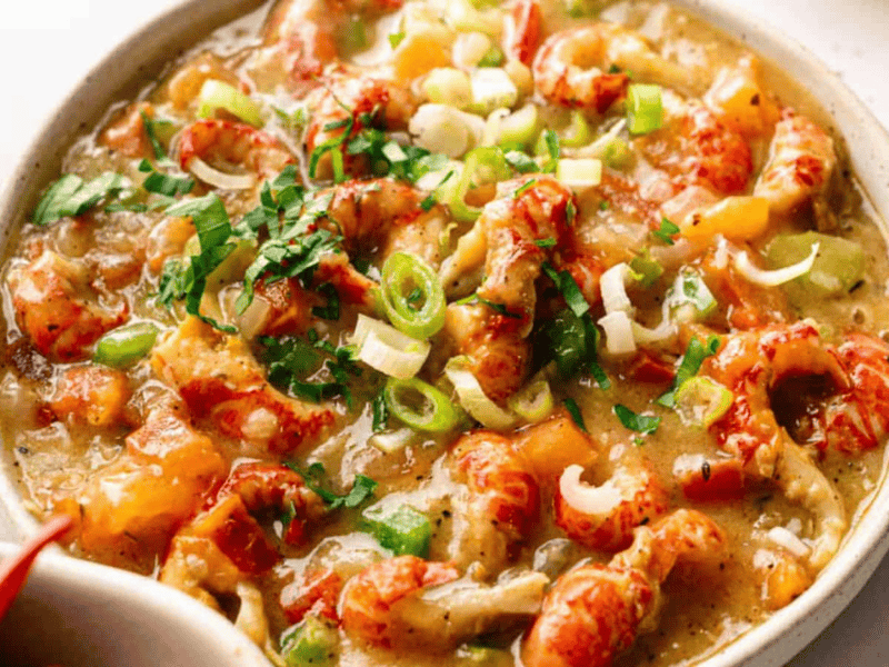 A bowl of crawfish &eacute;touff&eacute;e garnished with chopped green onions and herbs, served in a light-colored dish.