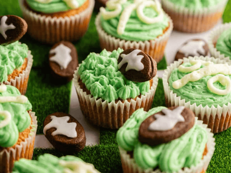 Cupcakes decorated with green frosting and chocolate footballs, arranged on a surface resembling a grass field.