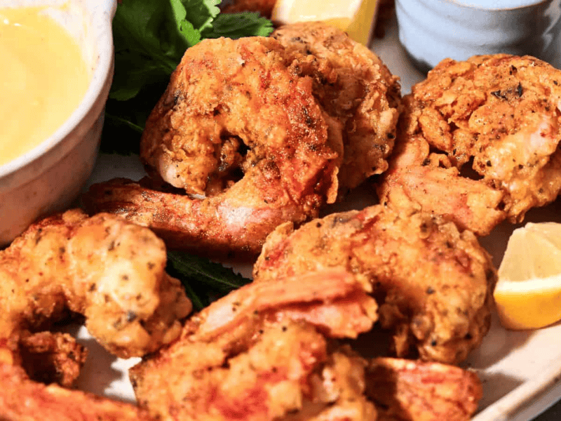 Close-up of a plate with fried shrimp, lemon wedges, and a bowl of dipping sauce.