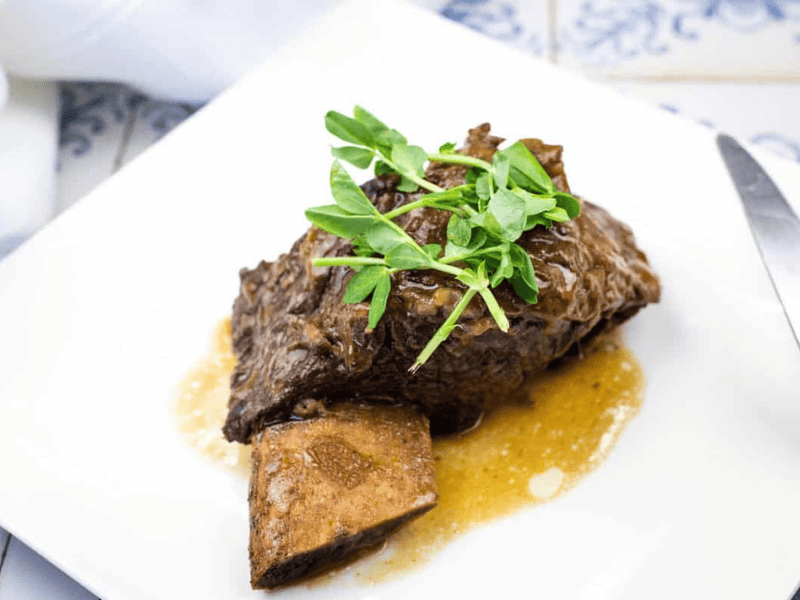 A Guinness-Braised Beef Short Ribs, garnished with parsley, served on a white square plate.