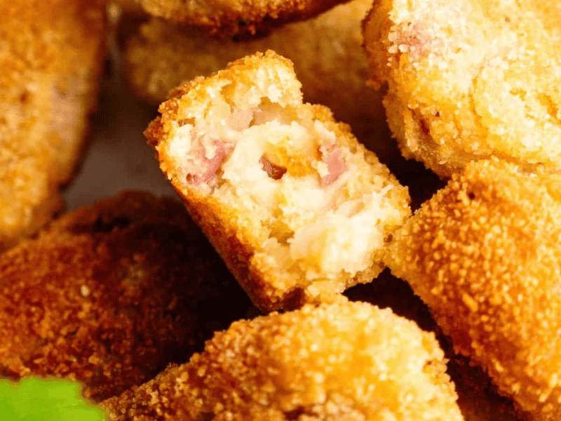 Close-up of breaded and fried croquettes, with one cut open to reveal a creamy filling mixed with diced ham.