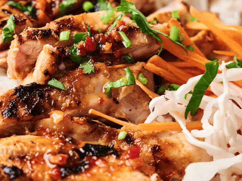 Grilled chicken with herbs on white rice, garnished with shredded carrots and cabbage.