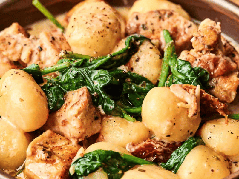 A bowl of gnocchi with pieces of chicken, wilted spinach, and a creamy sauce, garnished with black pepper.