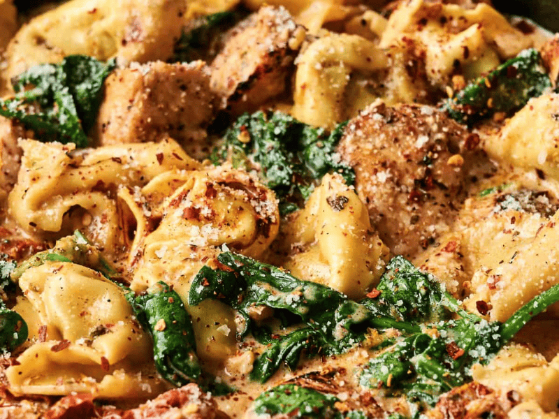Creamy tortellini pasta with spinach, grilled chicken slices, and a sprinkle of grated cheese and herbs.
