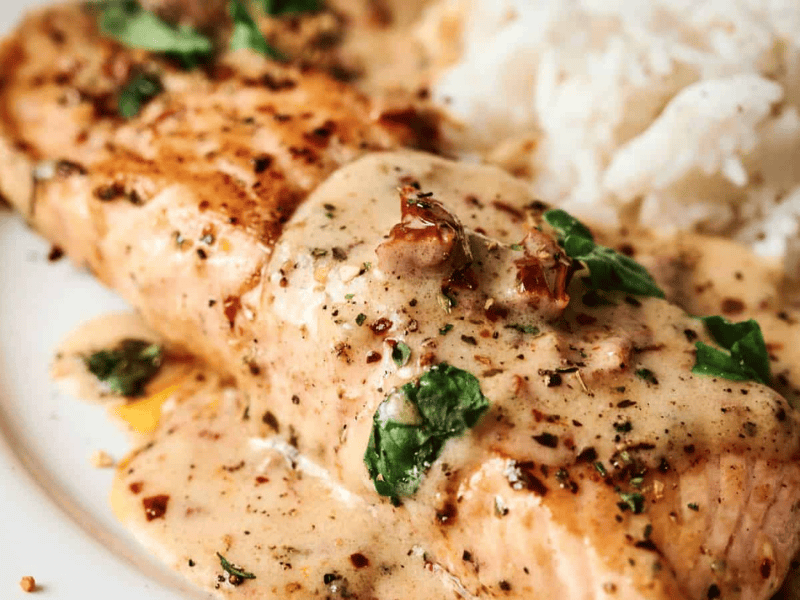 Grilled salmon fillet topped with a creamy herb sauce, served next to a portion of white rice.