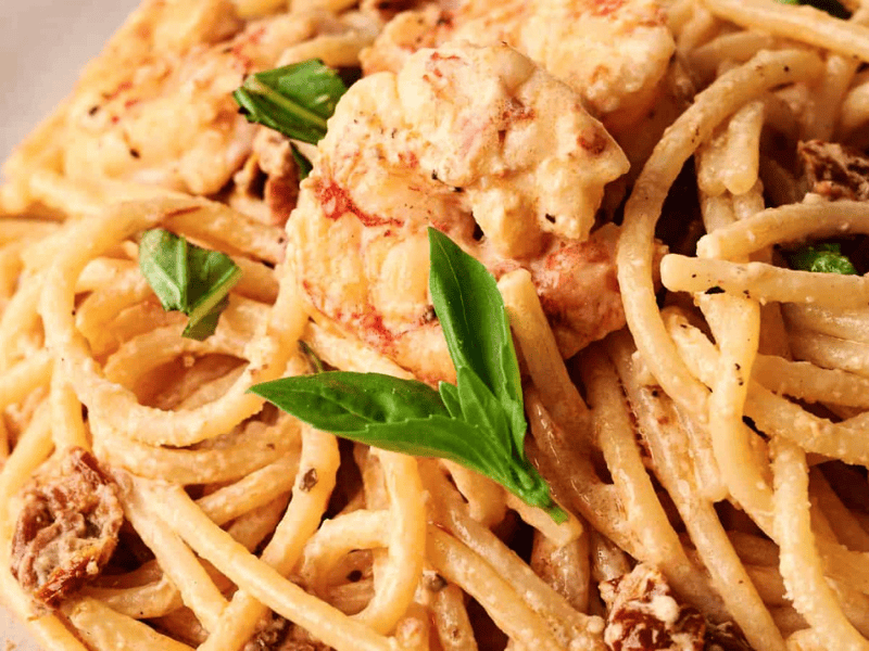 A plate of creamy spaghetti with shrimp, sun-dried tomatoes, and fresh basil leaves.