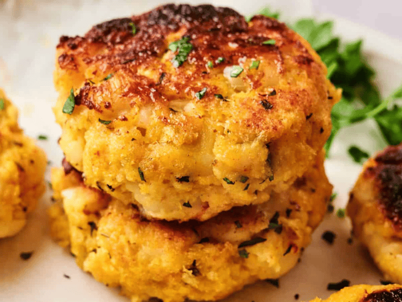 Close-up of golden-brown Maryland crab cakes garnished with herbs on a white plate, complemented by a fresh parsley garnish.