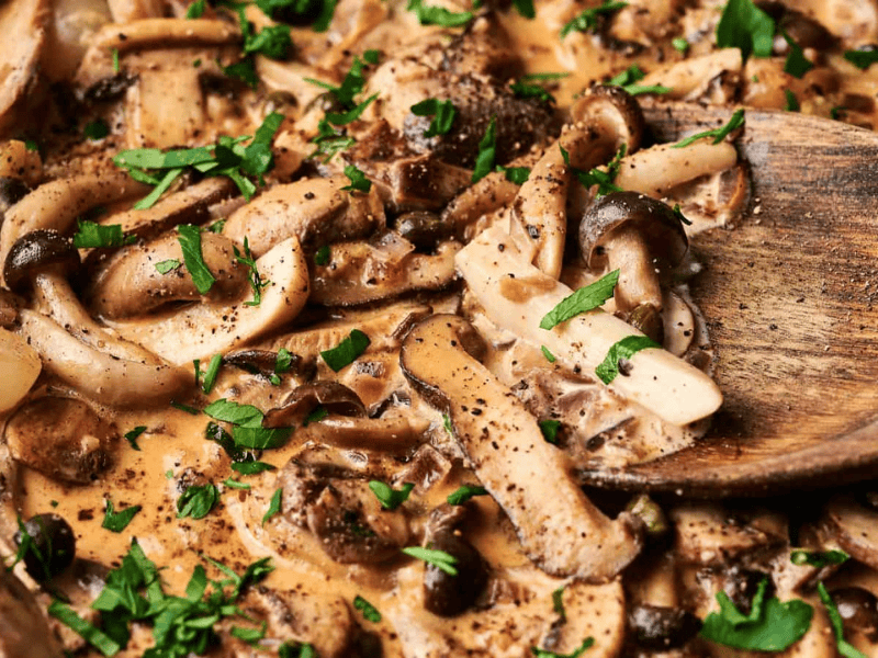 Creamy mushroom sauce with herbs and sliced mushrooms, stirred with a wooden spoon.