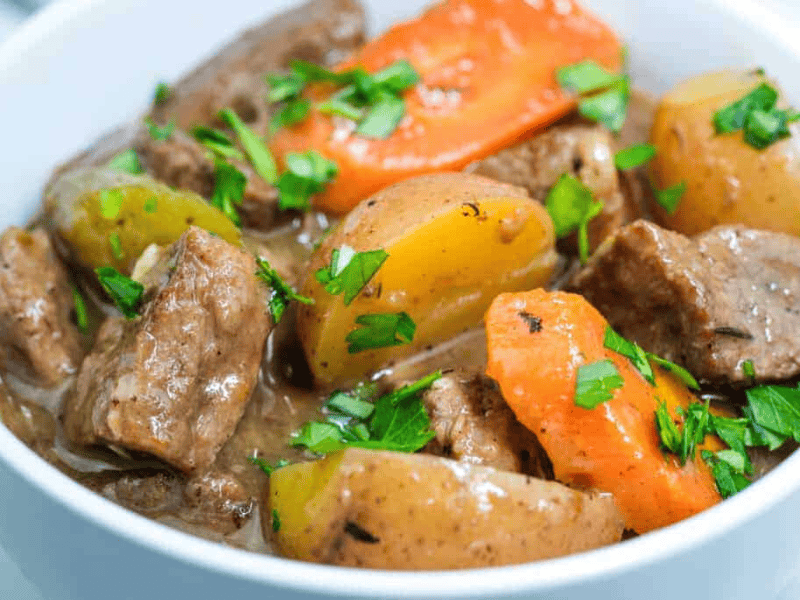 A bowl of old-fashioned beef stew garnished with fresh parsley.