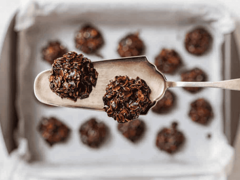 A metal spatula holds two chocolate Peanut Butter No-Bake Cookies above a baking tray lined with parchment paper and more cookies.