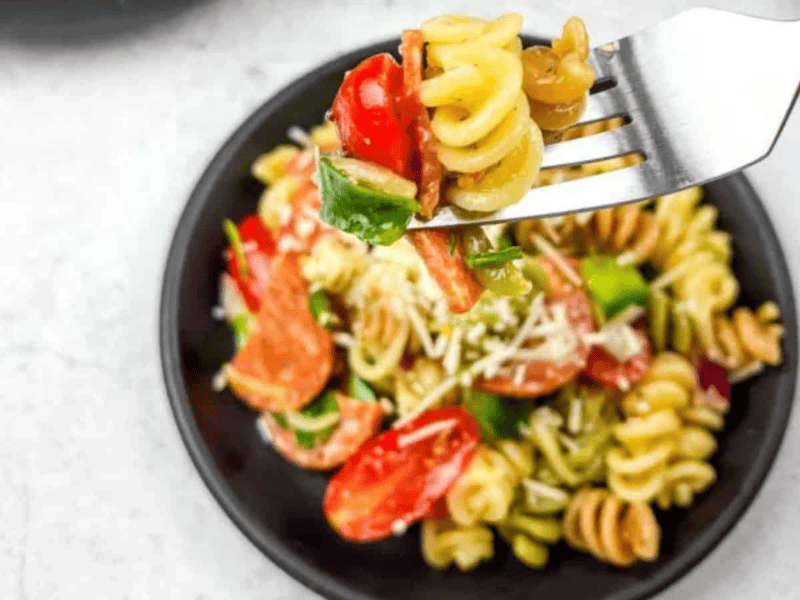 A fork with pizza pasta salad in a bowl.