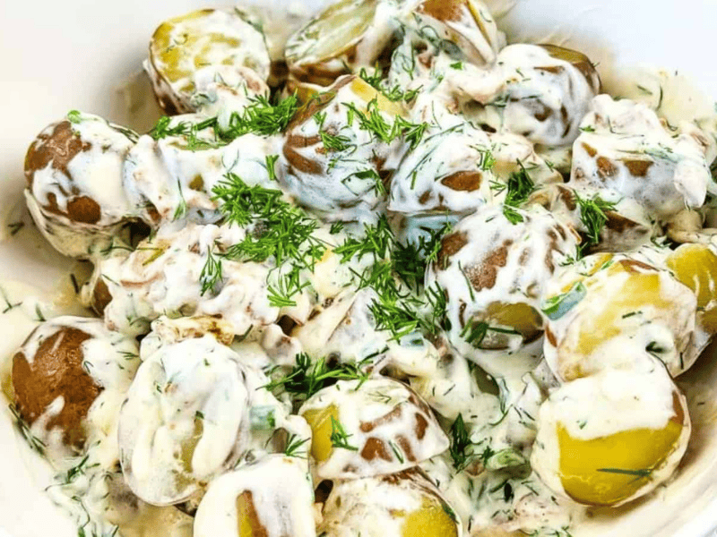 A bowl of boiled potatoes with skins on, topped with a creamy herb sauce and garnished with chopped fresh dill.