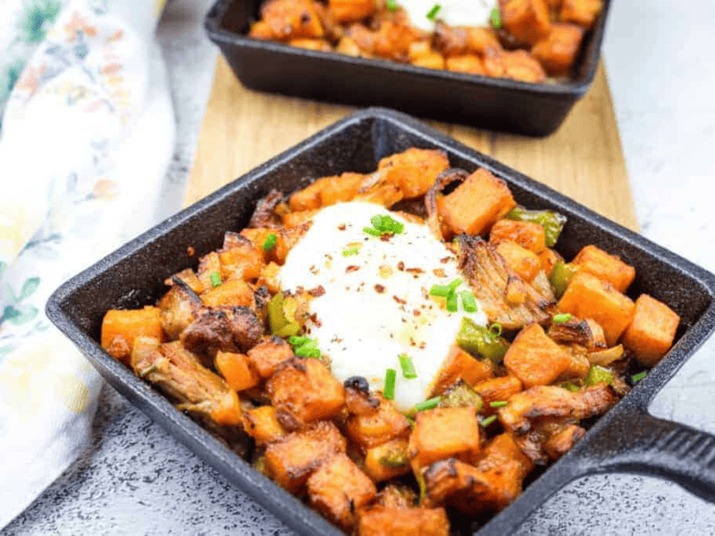 Cast iron skillet with sweet potato hash with pulled pork and garnished with chopped chives.