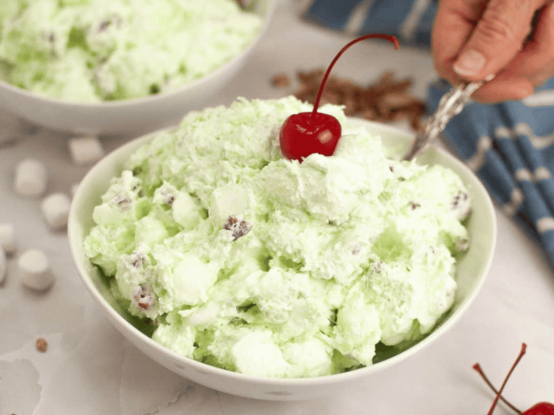 A bowl of Watergate salad topped with a cherry.