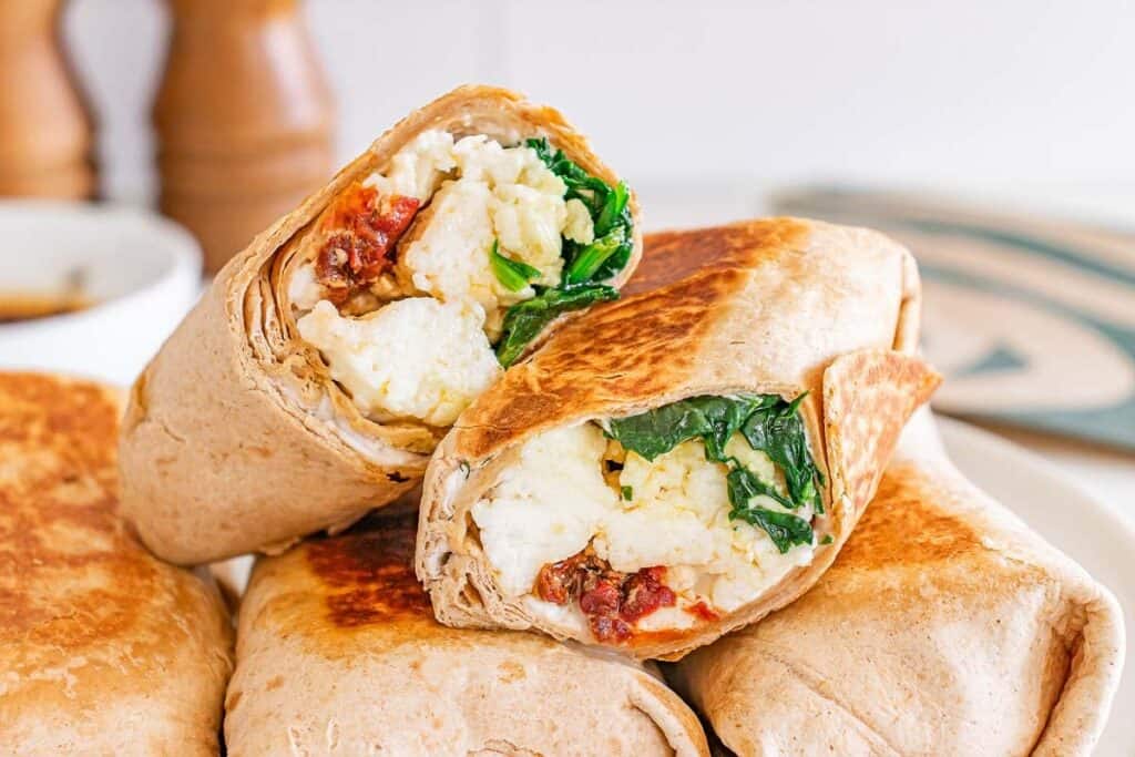 A close-up of breakfast burritos filled with scrambled eggs, spinach, and sun-dried tomatoes, stacked on a plate&mdash;perfect for anyone who loves Starbucks Copy Cat Recipes.