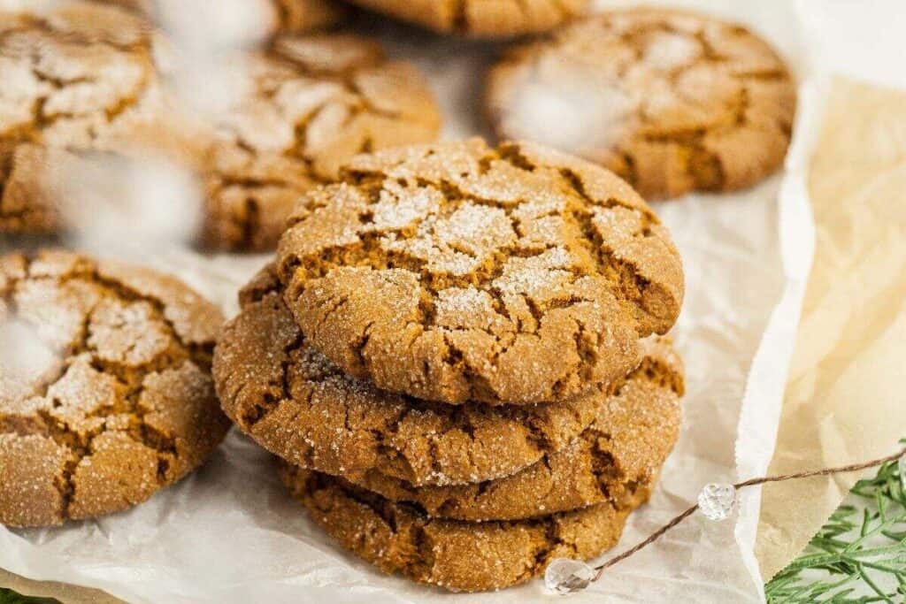 A stack of three sugar-coated ginger cookies sits on parchment paper, with more cookies blurred in the background&mdash;perfect for anyone searching for delicious Starbucks Copy Cat Recipes.