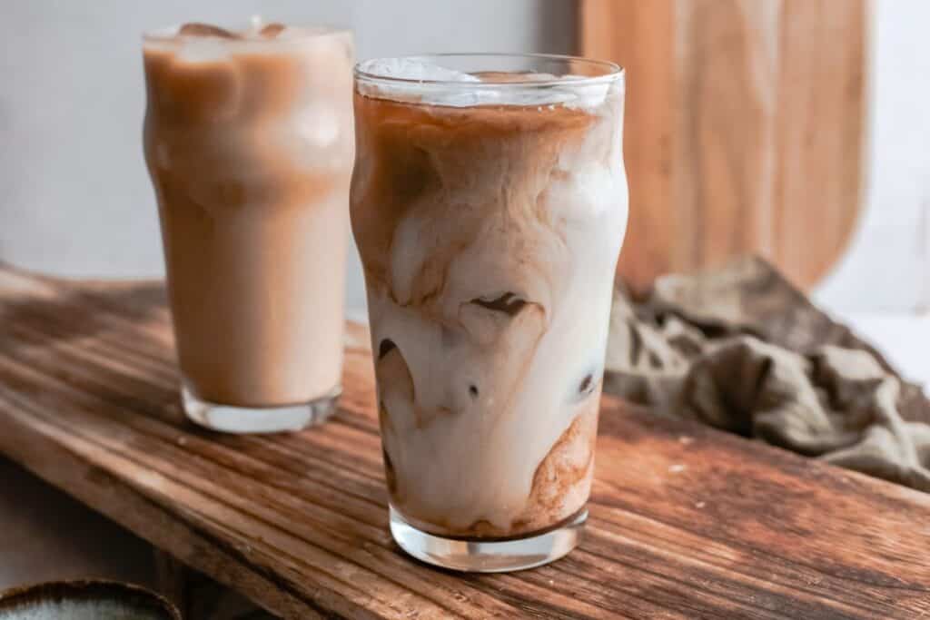 Two glasses of iced coffee with milk sit on a wooden surface; one boasts beautiful swirls where the milk meets the coffee, while the other appears more blended&mdash;perfect for trying your favorite Starbucks Copy Cat Recipes at home.