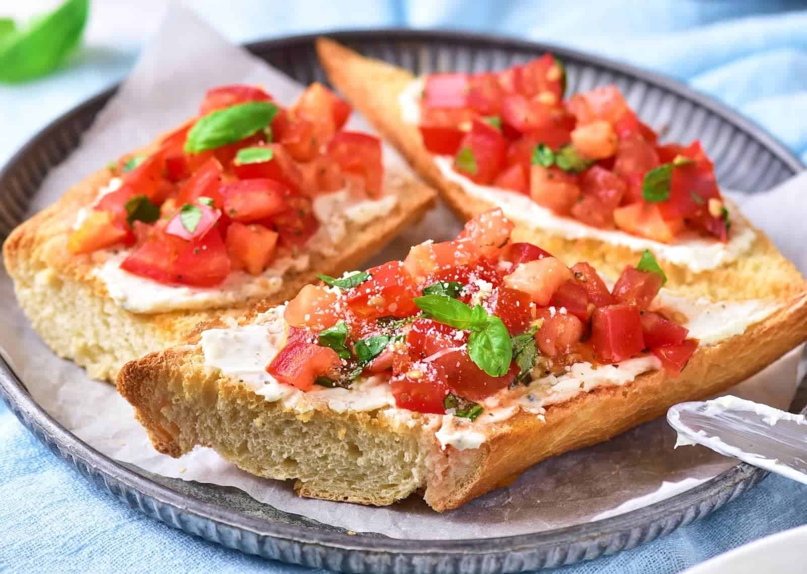 Three slices of toasted bread topped with a tomato mixture, herbs, and grated cheese are arranged on a round plate lined with parchment paper.