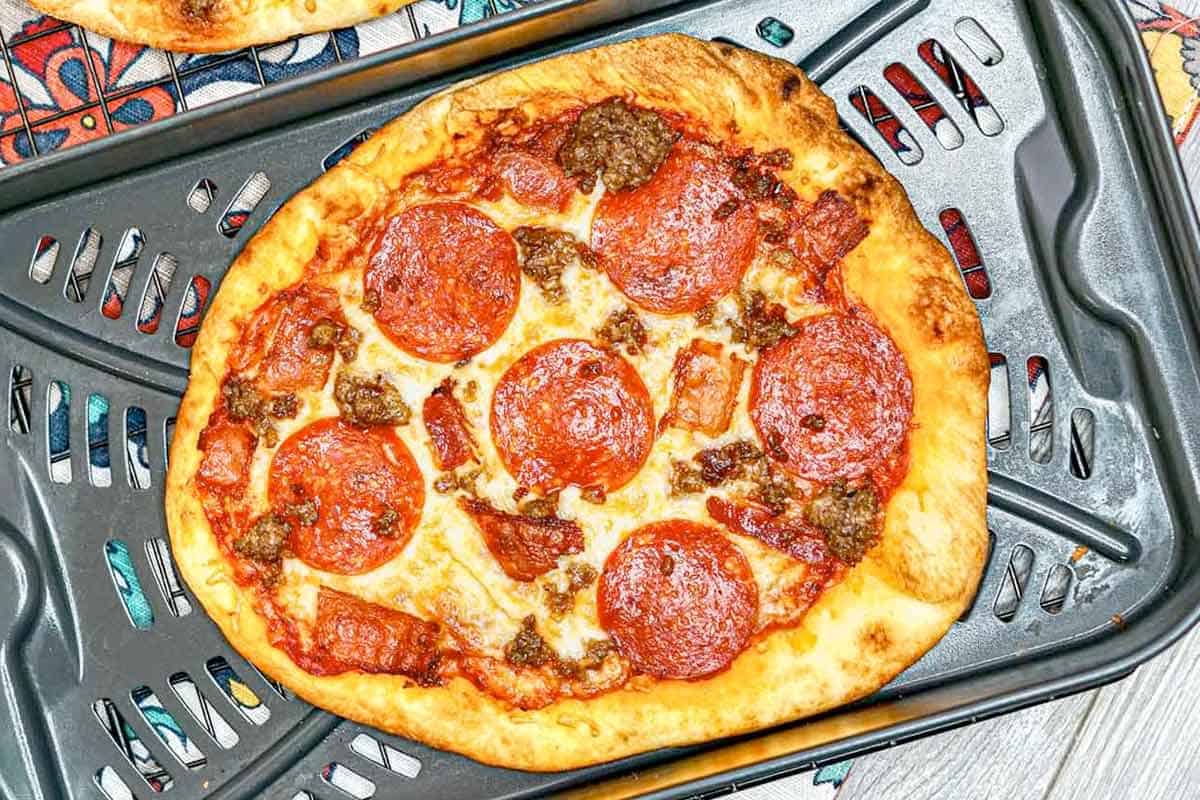 A cooked pizza with pepperoni, sausage, and bacon toppings on a metal baking sheet.