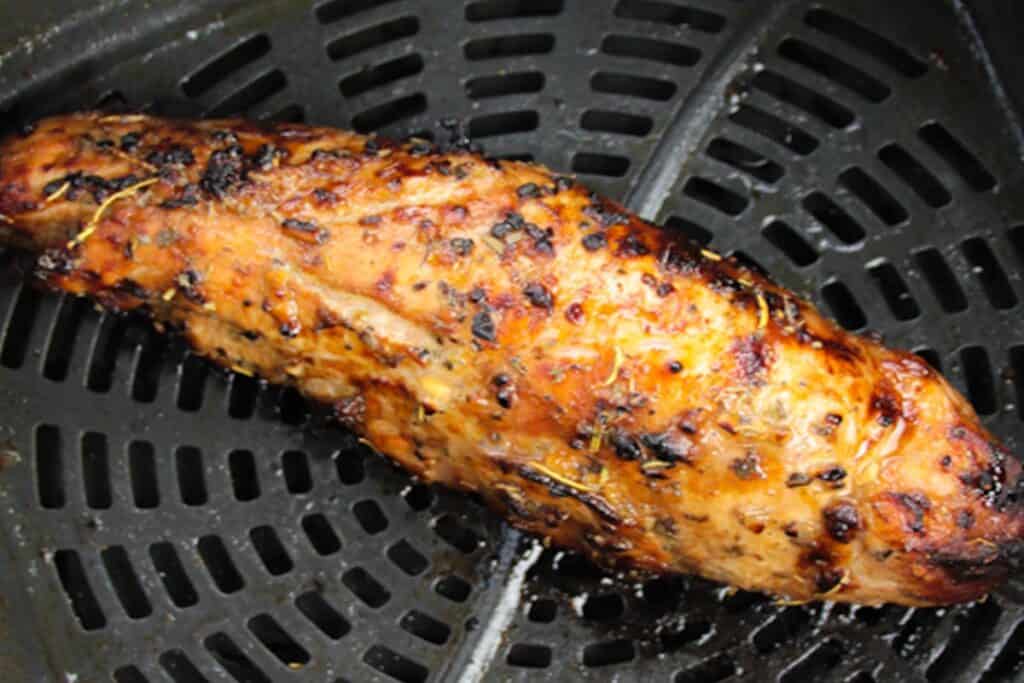 A cooked, seasoned pork tenderloin resting in an air fryer basket.