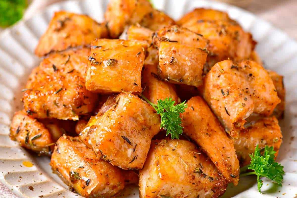 A plate of seasoned, roasted salmon bites garnished with fresh parsley.