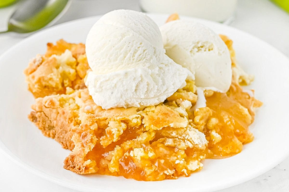 A serving of peach cobbler topped with two scoops of vanilla ice cream on a white plate.
