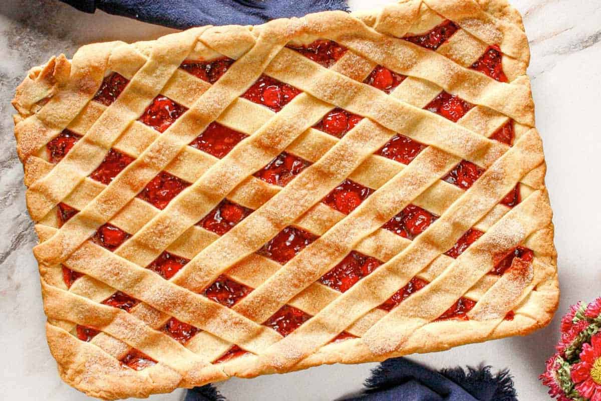 Rectangular cherry pie with a golden, lattice crust on a marble surface, showing glossy red filling through the openings.