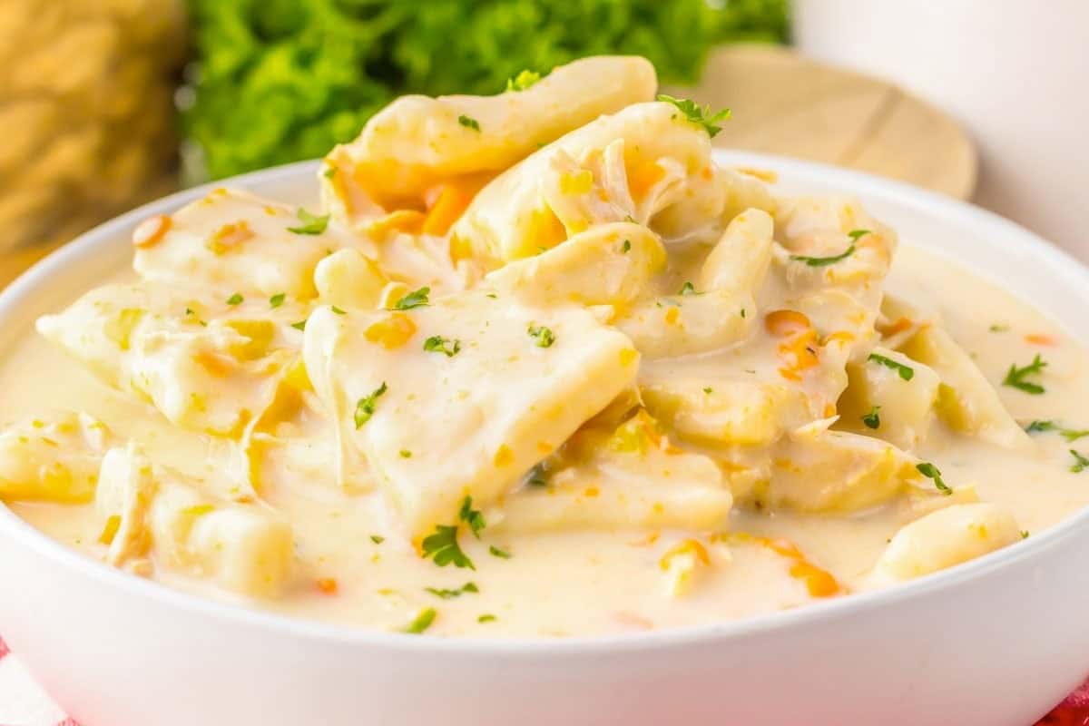 A bowl of creamy chicken and dumplings garnished with chopped parsley, with pieces of chicken and dumplings in a thick, white sauce.