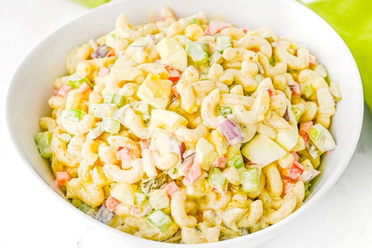 A bowl of macaroni salad with chopped vegetables and hard-boiled eggs in a creamy dressing.