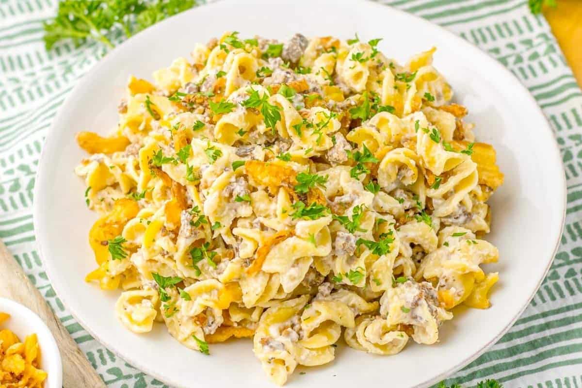 French onion beef casserole dish on a plate showcasing the creamy pasta with ground beef, features crispy fried onions on a striped green and white tablecloth.